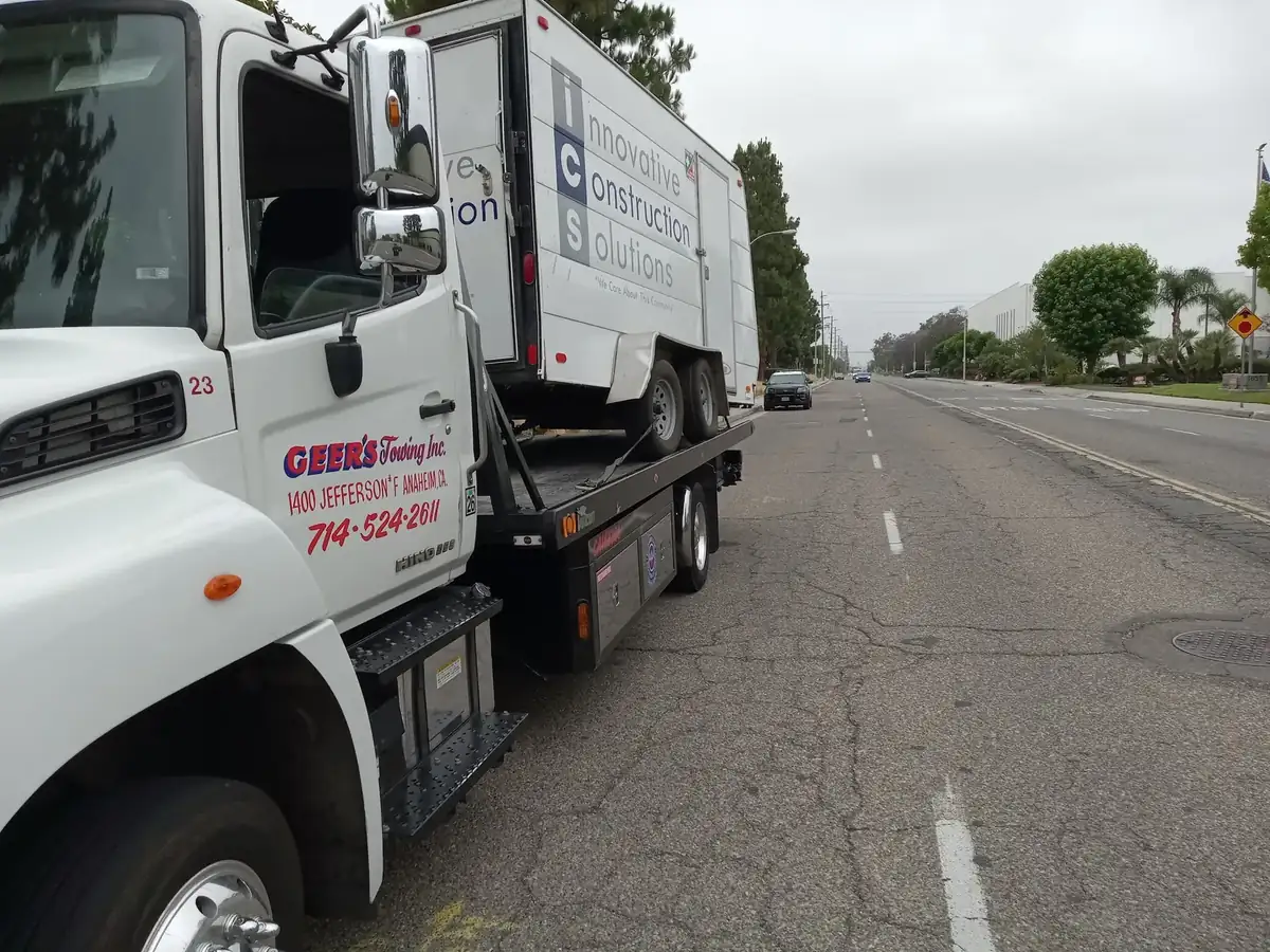 Geer's Towing Hino flatbed transporting a commercial box truck through Orange County