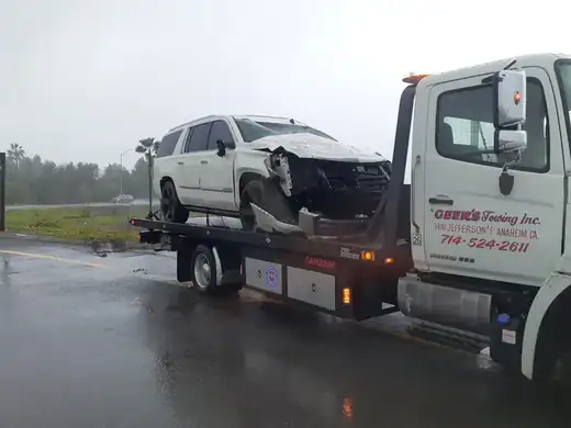 Geer's Towing flatbed recovering a wrecked Cadillac Escalade during rainy weather