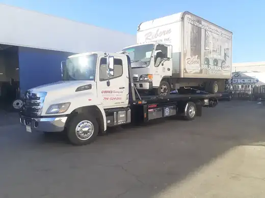 Geer's Towing Hino flatbed transporting a commercial delivery box truck