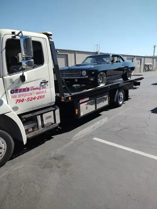 Geer's Towing flatbed transporting a classic Chevrolet Camaro muscle car