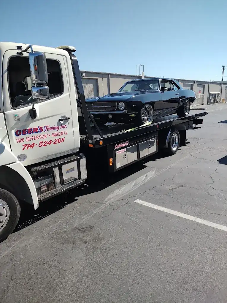 Geer's Towing flatbed transporting a classic Chevrolet Camaro muscle car